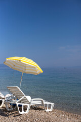 Two white sun loungers and yellow sun umbrella stand on the beach, vertical orientation