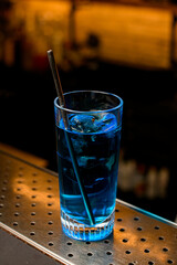 Close-up of clear glass of blue cold drink with drinking straw on bar