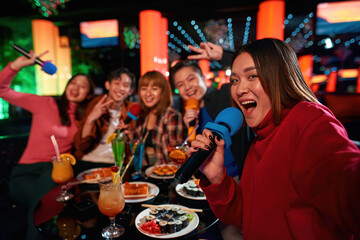 Group of asian guys and girls singing songs and making selfie at karaoke club