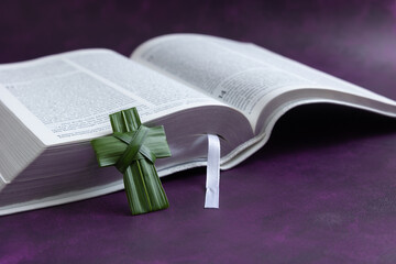 Palm leaf cross resting on an open bible on a dark purple background with copy space