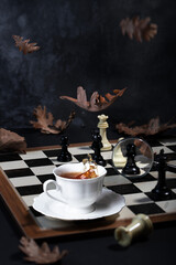 A cup of tea with a splash, falling autumn leaves on a chess table
