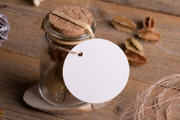 Round white tag mockup on glass jar with dry perfume a wooden background with boho decoration, element for packing. Label product mockup and natural eco design. Bohemian wedding gift, wedding favors