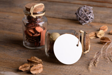 Round white tag mockup on glass jar with dry perfume a wooden background with boho decoration, element for packing