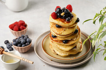 Fitness blueberry pancakes with protein, raspberries and walnuts stacked on top of each other on light grey background
