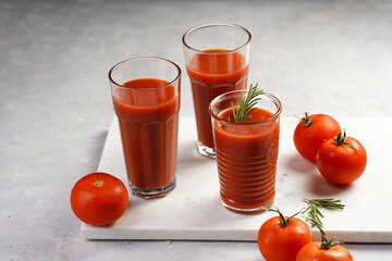 Several glasses full with red non-alcoholic tomato juice on marble plate on light grey background