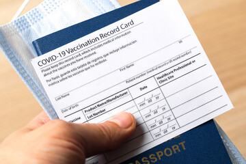 Fototapeta na wymiar Passport with COVID-19 Vaccination record card and medical mask in hand. Close up view. - Image