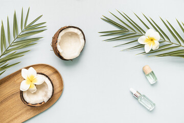 Obraz na płótnie Canvas Coconut essential oil and palm leaf oil on a table with copy space on a pastel background. Styled composition of flat lay with tropical leaves and flowers.