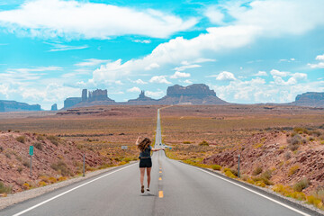 Fototapeta premium Attractive young woman from back view running in the middle of American straight road in the desert.