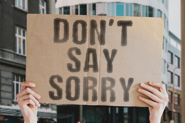 The phrase " Don’t say sorry " on a banner in men's hand with blurred background. Study. Shame. Wrong. Guilt. Final. Offer. Feel. Action. Choice. Sad. Good. Excuse. No. Career. Back. Despair. Upset
