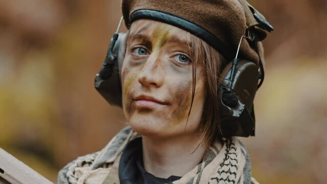 Portrait of an confident female soldier with headphones and face paint camouflage. High quality 4k footage