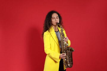 Beautiful African American woman playing saxophone on red background