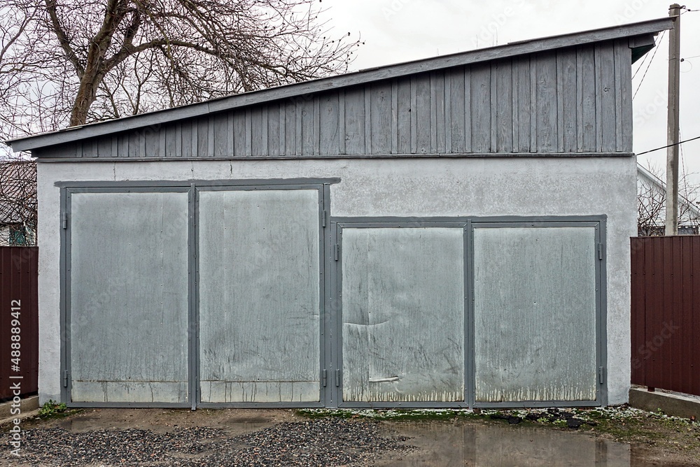 Poster facade of a rural garage with two gray metal gates on the street