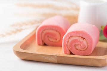 Pink strawberry roll cake or swiss roll with whipped cream and strawberry flavor on wooden plate