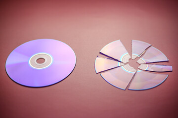 Broken compact disc divided into parts and a whole compact disc close-up on a red-burgundy...