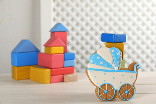 Tasty cookie in shape of stroller and colorful cubes on white wooden table, space for text. Baby shower party