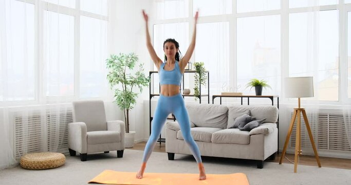 Young woman doing jumping jack exercise at home