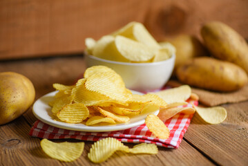 Potato chips snack on white plate, Crispy potato chips on the kitchen table and fresh raw potatoes