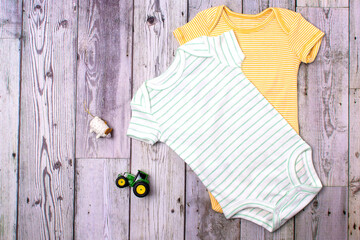 yellow and green bodysuit made of cotton with a children's toy. Clothes for newborns on a gray background. copy space.