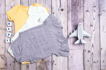 Fototapeta na wymiar yellow bodysuit, gray bodysuit and green cotton bodysuit with baby toy and cubes. Clothes for newborns on a gray background.