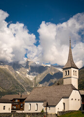 Fototapeta na wymiar The church of the Swiss town Bellwald in the canton of Valais, with mountains and impressive cloud formations in the background