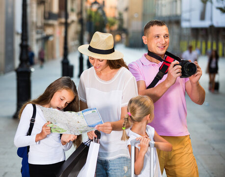 Happy cheerful smiling tourist family using map and taking photo of city while strolling with camera and phone