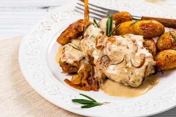 Rabbit Meat With Rosemary in Sour Cream Sauce and Potato on White Wooden Background. Selective focus.