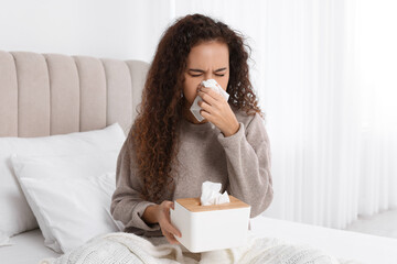 Sick African American woman with box of paper tissues suffering from cold in bed at home