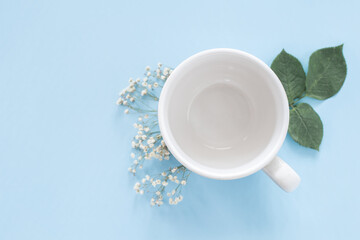 Taza blanca vacía para montar té o café con temática primaveral sobre fondo azul cielo