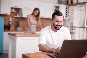 young man uses laptop in home kitchen