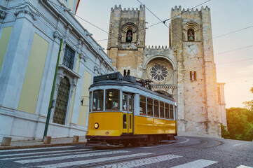 Typical yellow tram going up the Alfama district in front of Lisbon cathedral - Portugal. - obrazy, fototapety, plakaty
