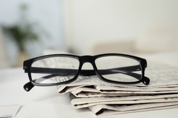 Stack of newspapers and glasses on white table indoors