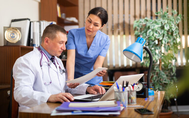 Two doctors man and woman analysing and consulting over medical record in modern hospital