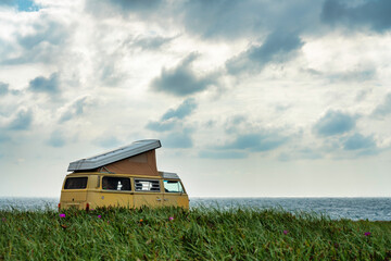 Yellow camper van standing in front of the sea on a cliff with dramatic sky.