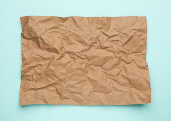 Sheet of crumpled brown paper on light blue background, top view