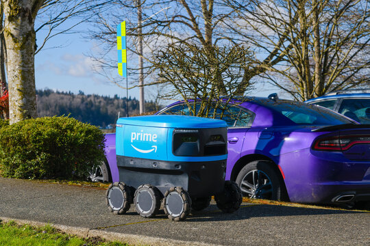 Monroe, WA, USA - February 21, 2022; Amazon Prime Autonomous Scout Robot Delivery Device On Sidewalk Passing Parked Cars