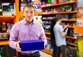 Interested adult man shopping in store of kids toys, holding carton with new plaything