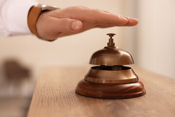 Man ringing service bell at wooden reception desk in hotel, closeup