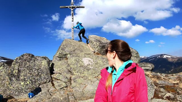 A happy Couple at the summit cross of Seinerkreuz on Packsattel, Styria in the Austrian Alps. Man runs up to the peak, while the woman is filming the scene. Wanderlust. Hirschegger-Alm. Good emotion
