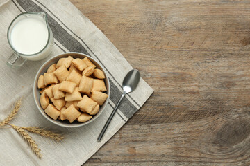 Bowl of sweet crispy corn pads and milk on wooden table, flat lay with space for text. Breakfast cereal