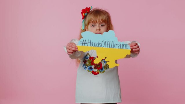 Portrait of Ukrainian girl child in embroidery dress showing banner with massage inscription text on map Hands Off Ukraine. Asking for help. Crisis, war, no peace, stop aggression from Russia country