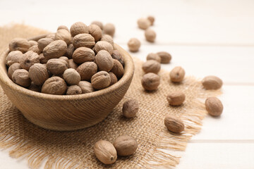 Scattered nutmeg seeds, bowl and sack cloth on white wooden table, closeup. Space for text