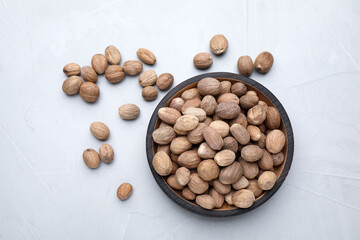Bowl with nutmeg seeds on light table, flat lay