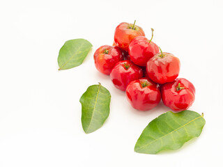 Pile of red acerola cherries and green leaves on a white background