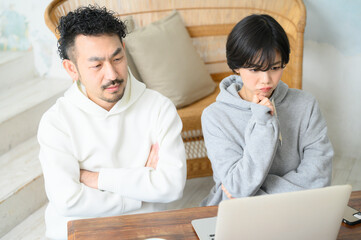 A couple looking at a computer and worrying with their arms crossed.