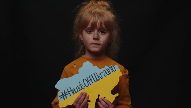 Upset poor toddler girl kid homeless with dirty face protesting war conflict raises banner with inscription massage text Hands Off Ukraine. Crisis, peace, stop Russian aggression, child against war
