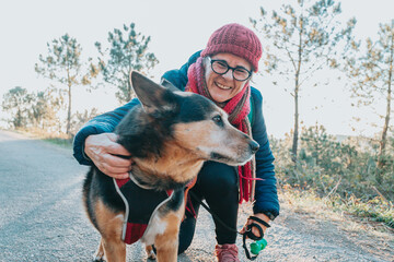 Old woman with his dog during a walk portrait wearing a hat for spring and winter smiling toc...