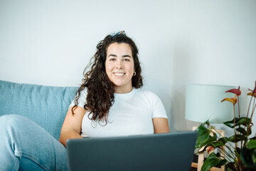 Happy plus size curly young woman smiling to camera while using a laptop to prepare,and do work...