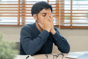 Entrepreneur exhausted, hand of stress asian young business man working in headache, suffer on hard work while use laptop computer at office. Overtime job, debt problem and despair people. Sick unwell