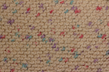 Full frame abstract texture background of hand knitted cotton yarn cloth in a simple garter stitch, in beige with scattered colors