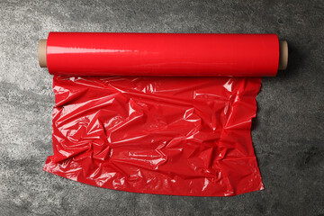 Roll of red plastic stretch wrap on grey stone background, top view